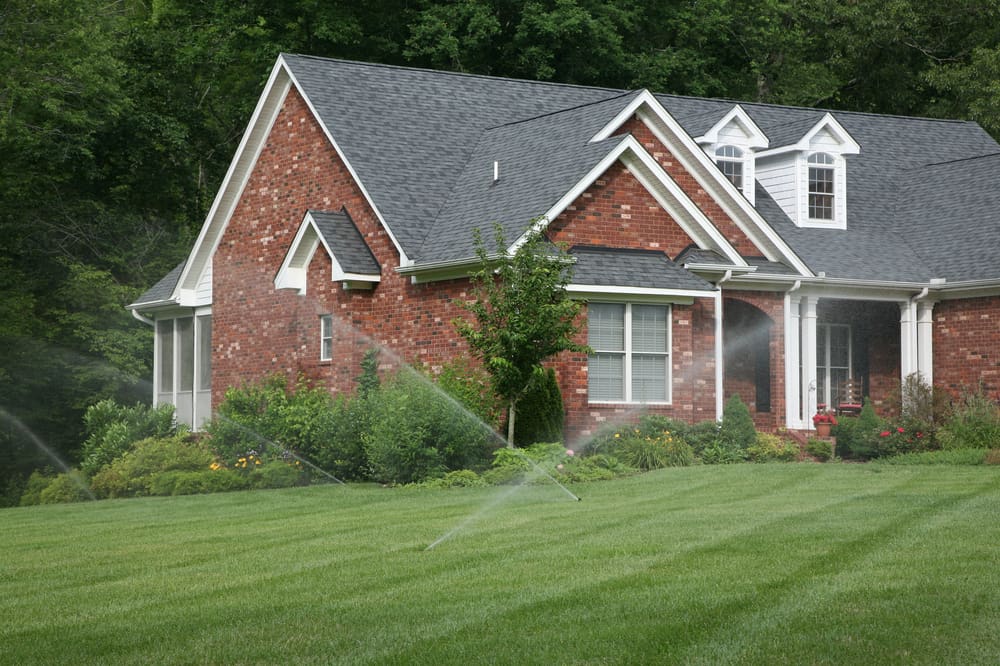 Front lawn of a brick home in Smyrna with sprinklers active, showcasing pest control Smyrna services in action.